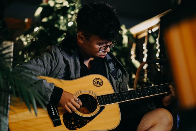 A young man sits playing an acoustic guitar.