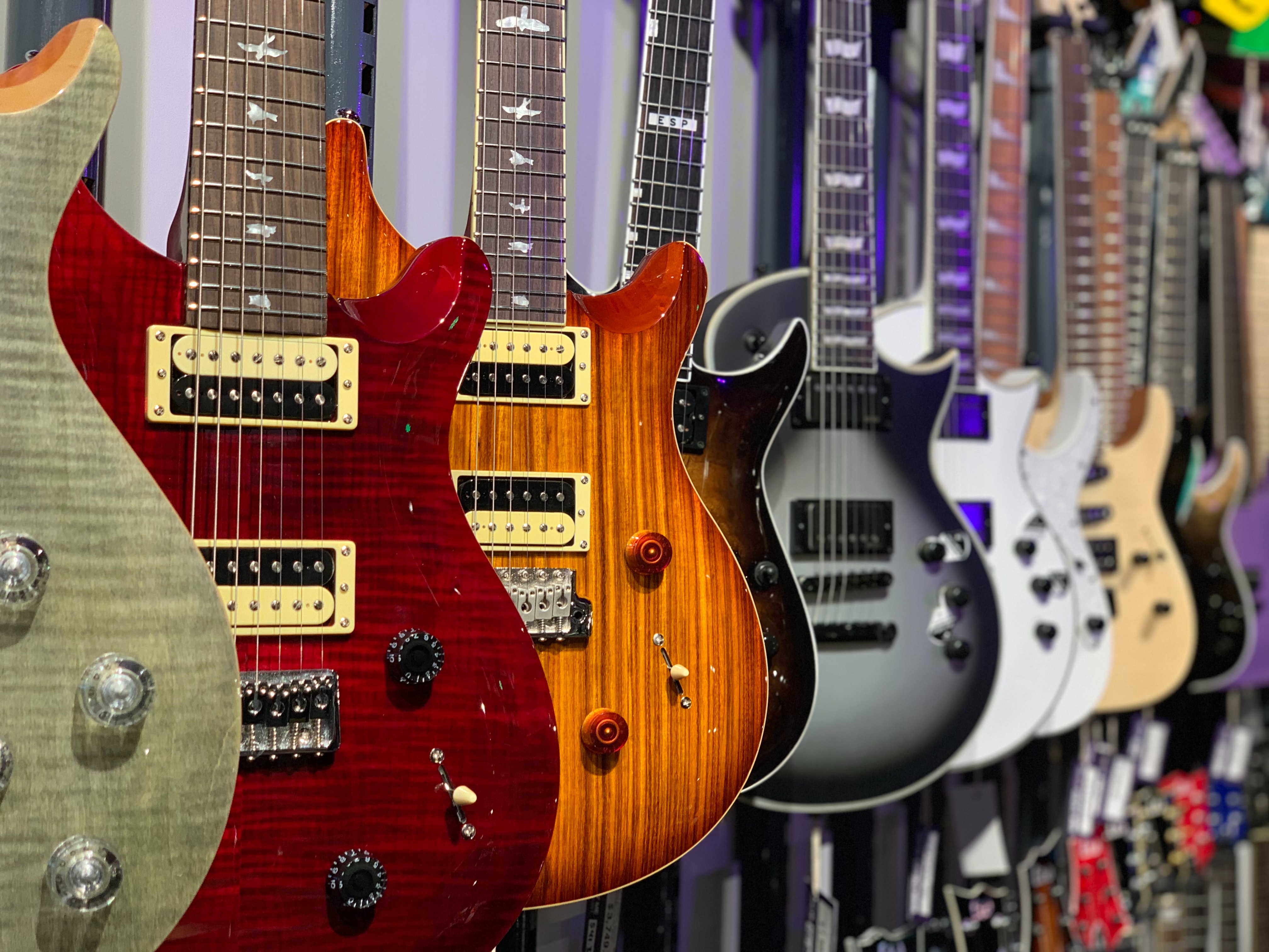 Electric guitars with varying finishes hanging from wall. These are some gorgeous guitars that sport both looks and tone!